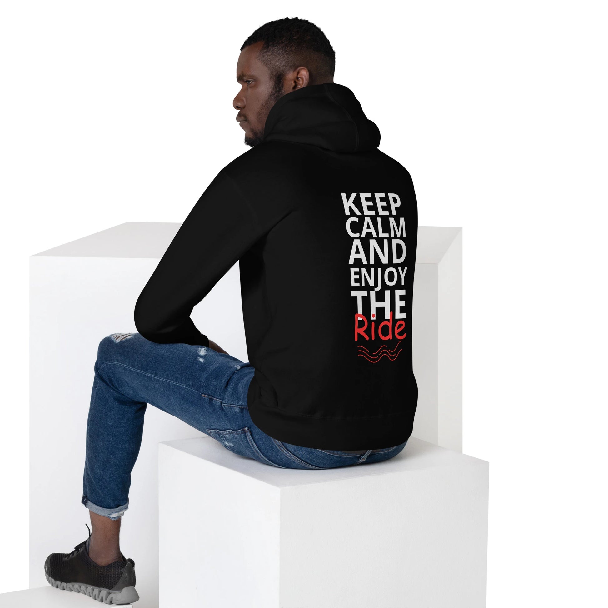 Flat lay of black hoodie on sitting man showing large vertical 'Keep Calm and Enjoy the Ride' print in white and red on the back.